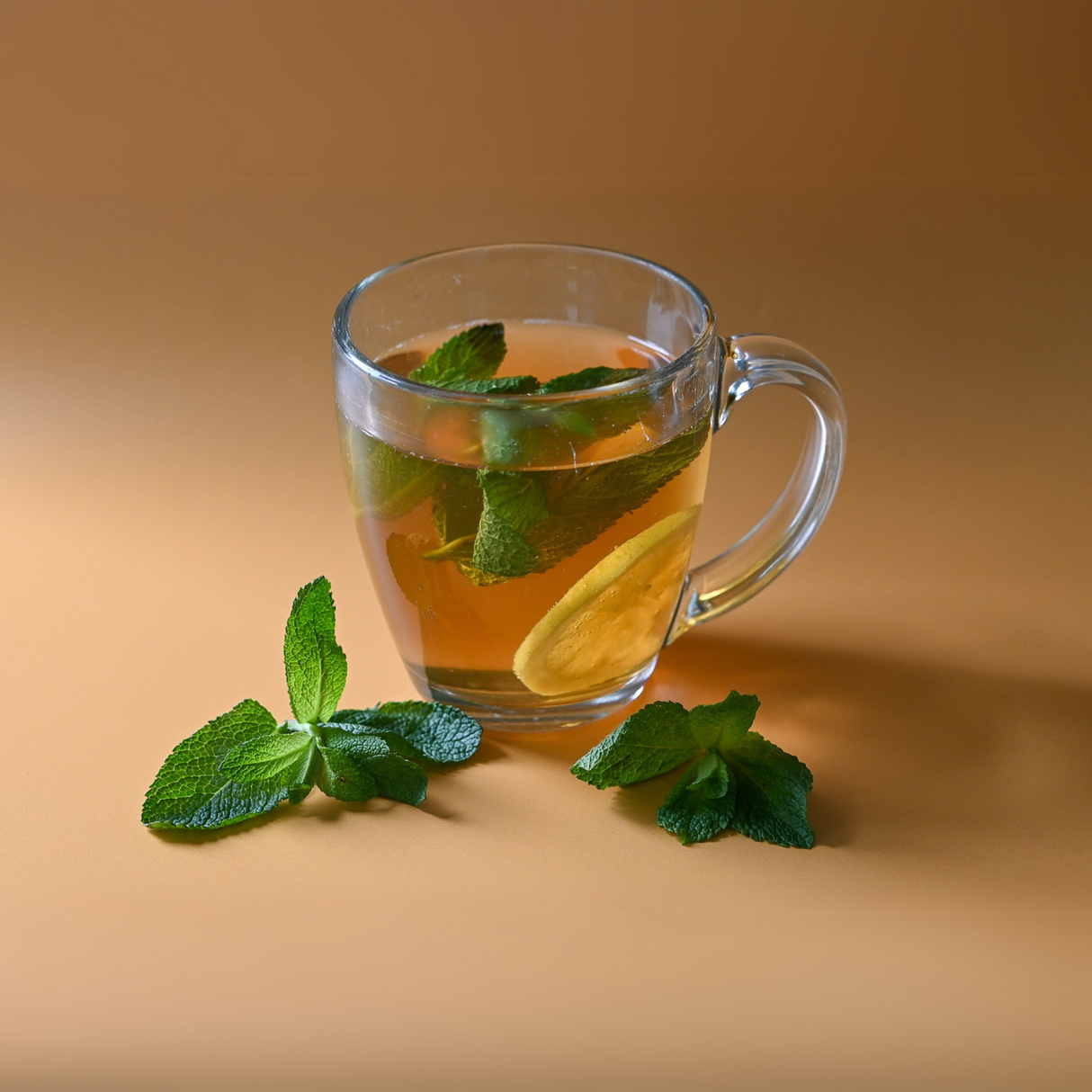 A caffeine-free glass mug of 100% Pure Peppermint Herbal Tea with mint leaves and a lemon slice, set on a brown background, captures the calming essence and health benefits of nature's remedy.