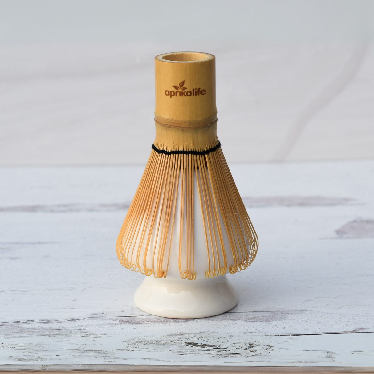 A bamboo matcha whisk on a white ceramic holder, part of the Beige Ceramic Matcha Bowl, Bamboo Matcha Whisk, Whisk Holder and Organic Japanese Matcha Set, crafted with Minoyaki pottery style, rests gracefully on a light wooden surface.