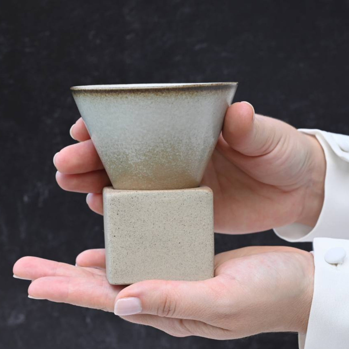Hands holding a Brown Coffee Mug with Base against a dark background, showcasing exquisite ceramic artistry.