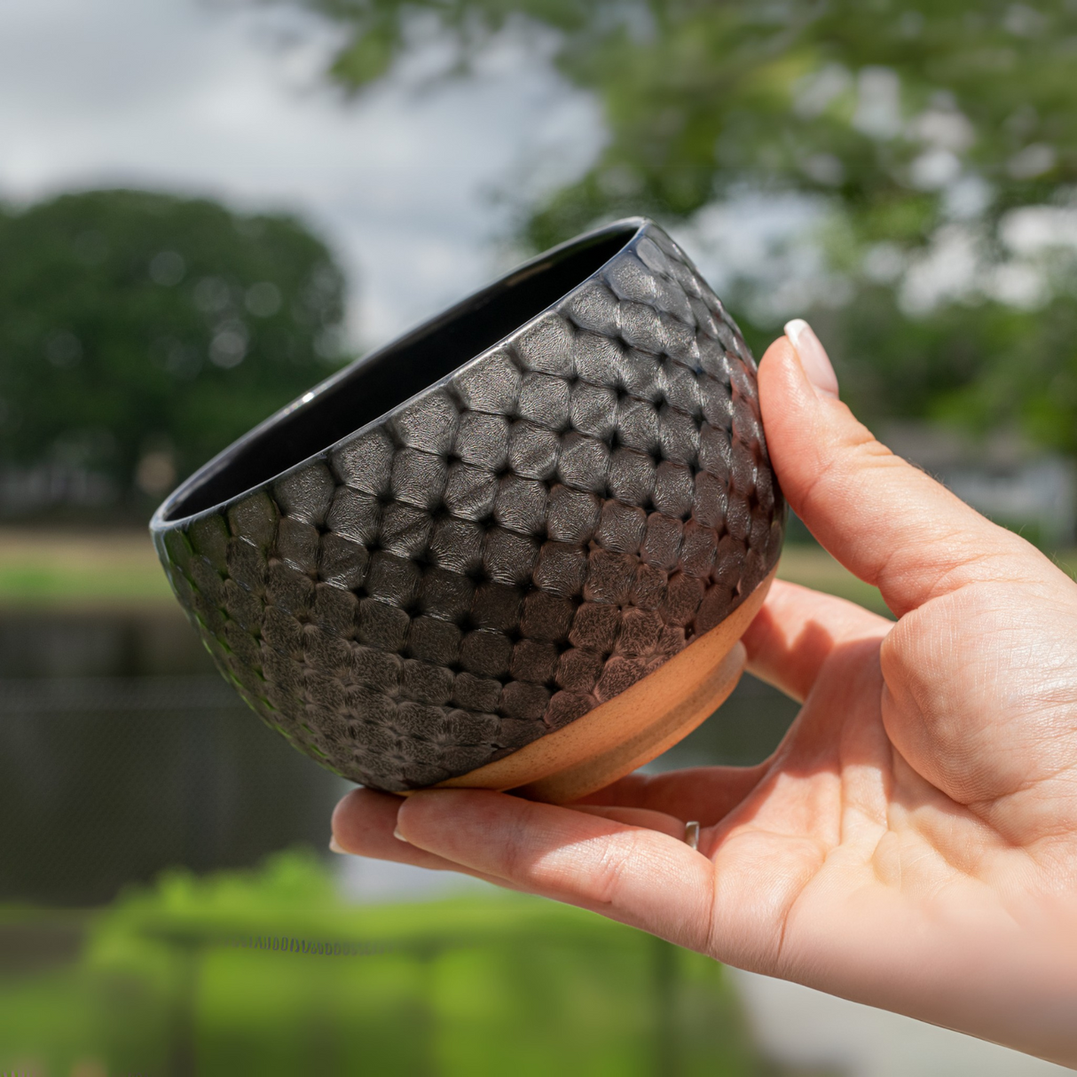 The Black Ami Pattern Set matcha bowl is gently cradled outdoors, with blurred greenery creating a serene backdrop.