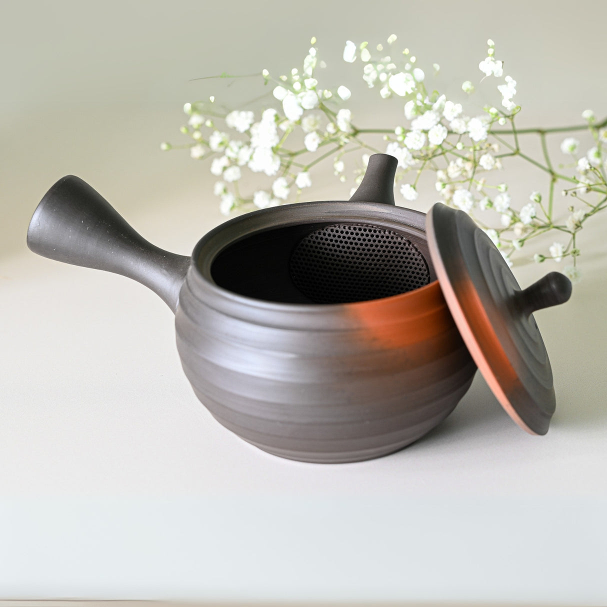 A Japanese Kyusu Set teapot, part of a 270ml set with filters and two cups, sits gracefully with its lid slightly ajar in front of delicate white baby's breath flowers.