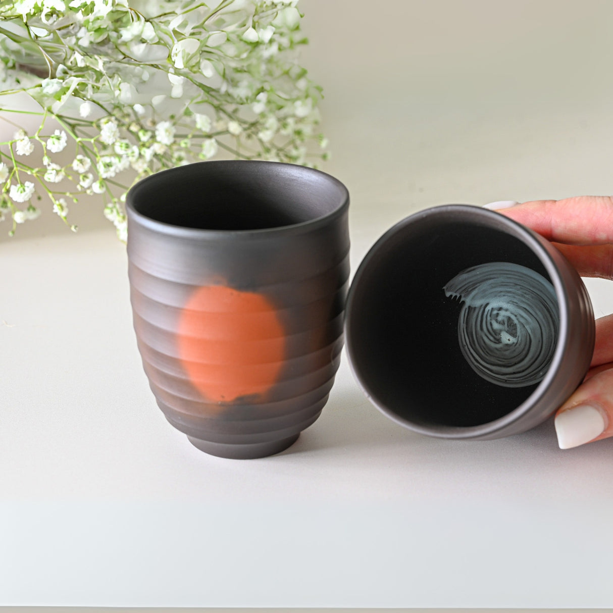 A Japanese Kyusu Set featuring a teapot with filters and two black Yunomi cups elegantly adorns the table, complemented by delicate white flowers in the background.