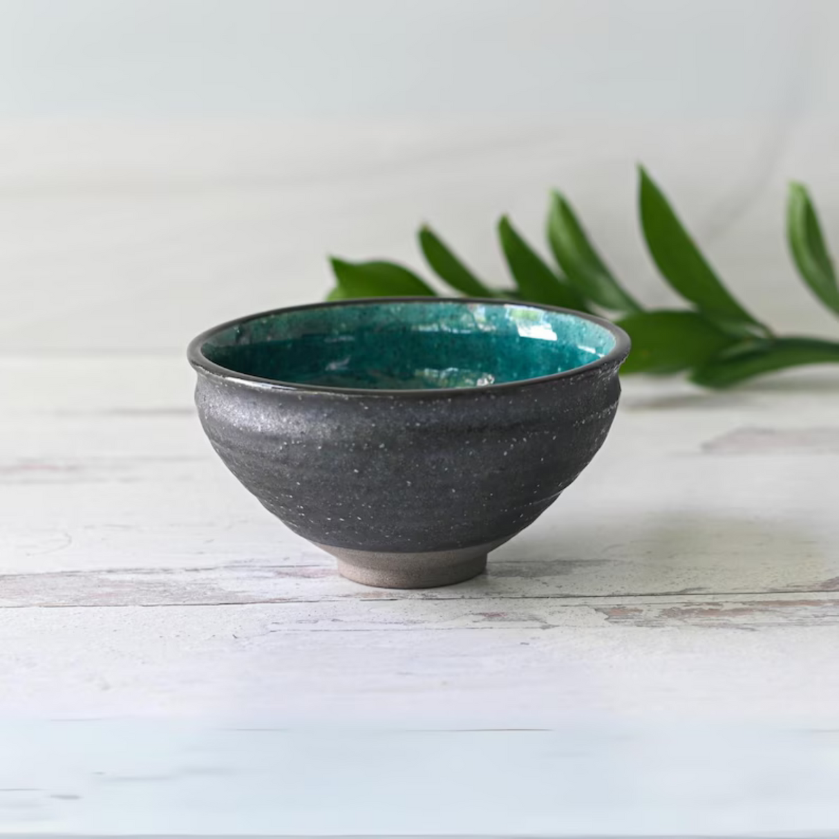 Blue and Black Ceramic Matcha Bowl on a white wooden surface, with green leaves in the background.