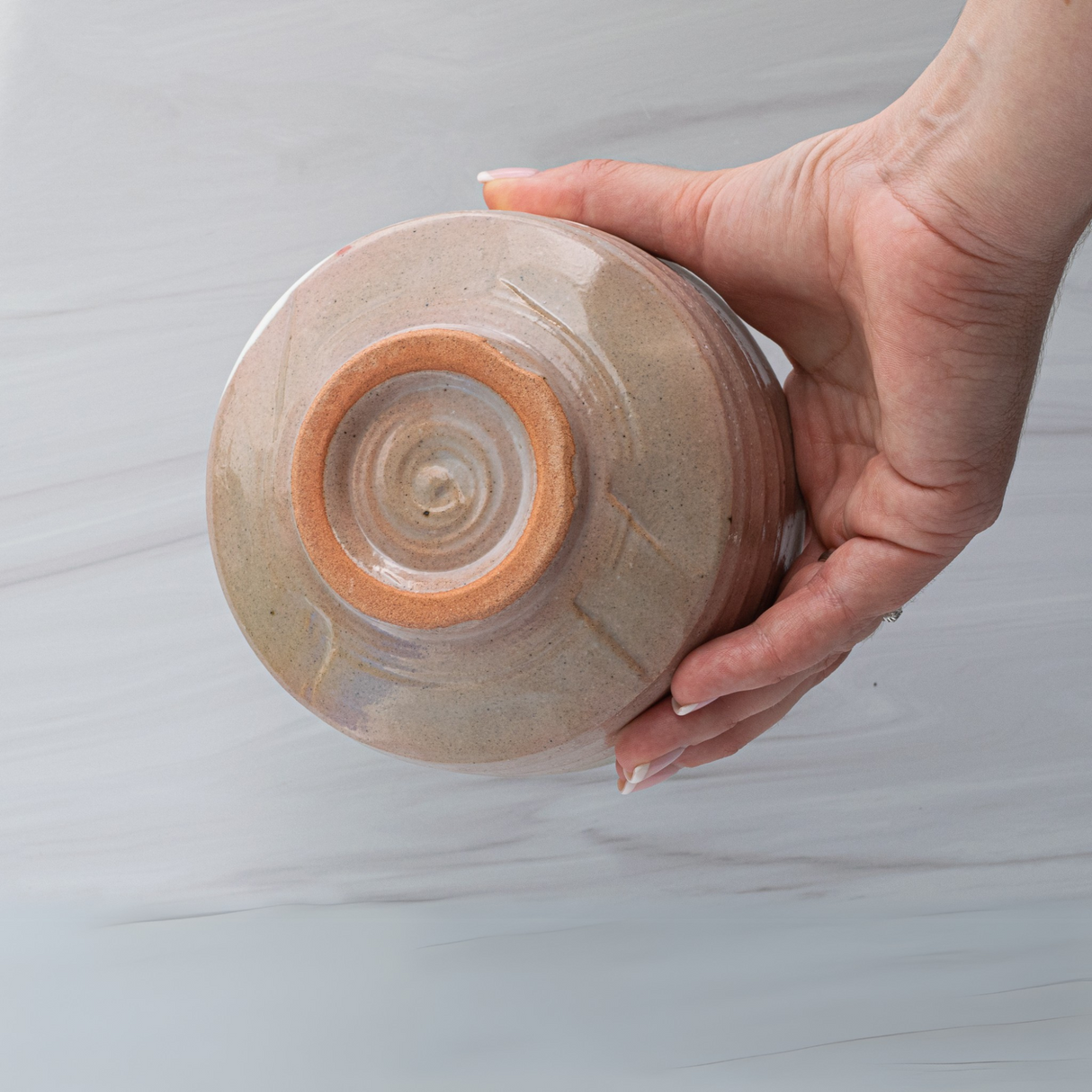 A hand holds the Big Sakura Flowers Matcha Bowl from the Matcha Set, displaying its natural, unglazed base against a light background and showcasing the refined beauty of Japanese pottery.