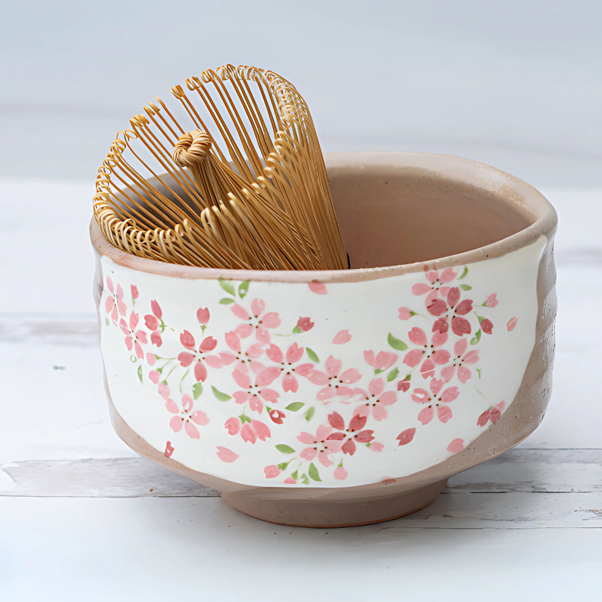 The Big Sakura Flowers Matcha Bowl, Bamboo Matcha Whisk, Whisk Holder, and Organic Japanese Matcha Set features a cherry blossom bowl with a bamboo whisk and holder, beautifully displayed on a light wooden surface.