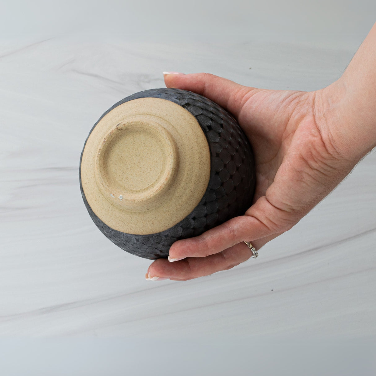 A hand holds an upside-down Black Ami Pattern Matcha Bowl against a light background, highlighting the elegance of Japanese pottery.