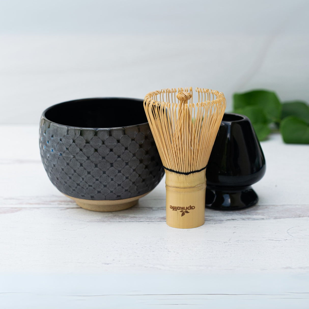 Black Ami Pattern Matcha Bowl, bamboo whisk, and holder elegantly arranged on a wooden surface with a soft background.