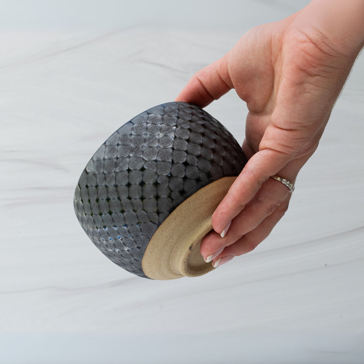 A hand gently cradles the Black Ami Pattern Matcha Bowl, a textured ceramic piece reminiscent of classic Minoyaki craftsmanship with an intricate woven design, elegantly standing out against a light background.