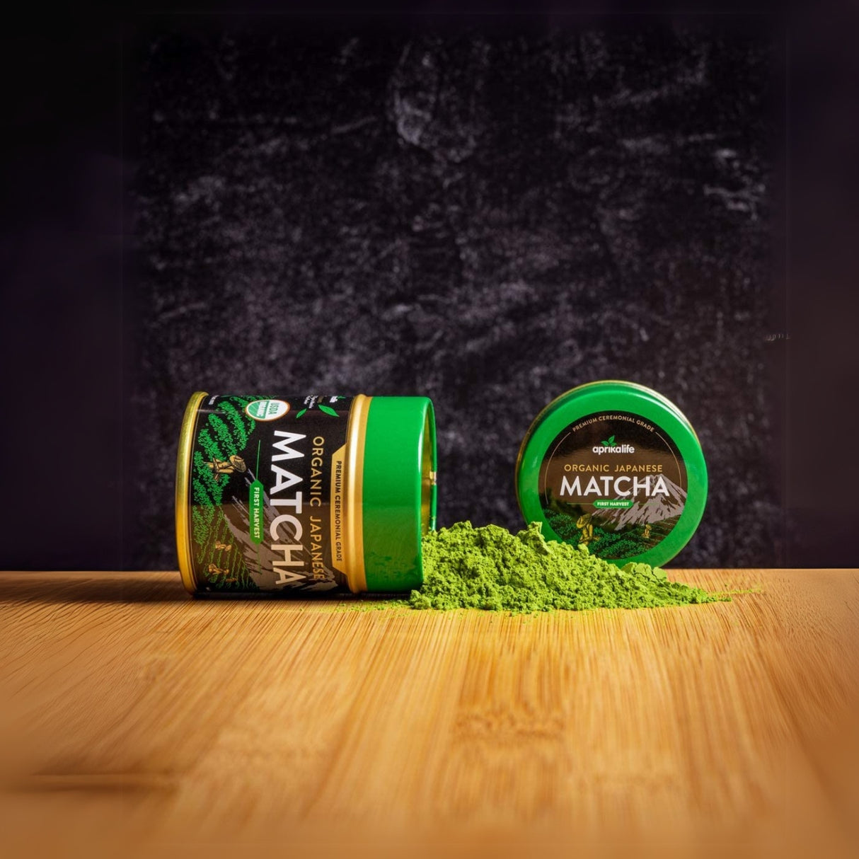 Matcha powder elegantly spills from a tipped container onto a wooden surface, with a closed container suggesting the complete Black Matcha Tea Gift Set in the background.