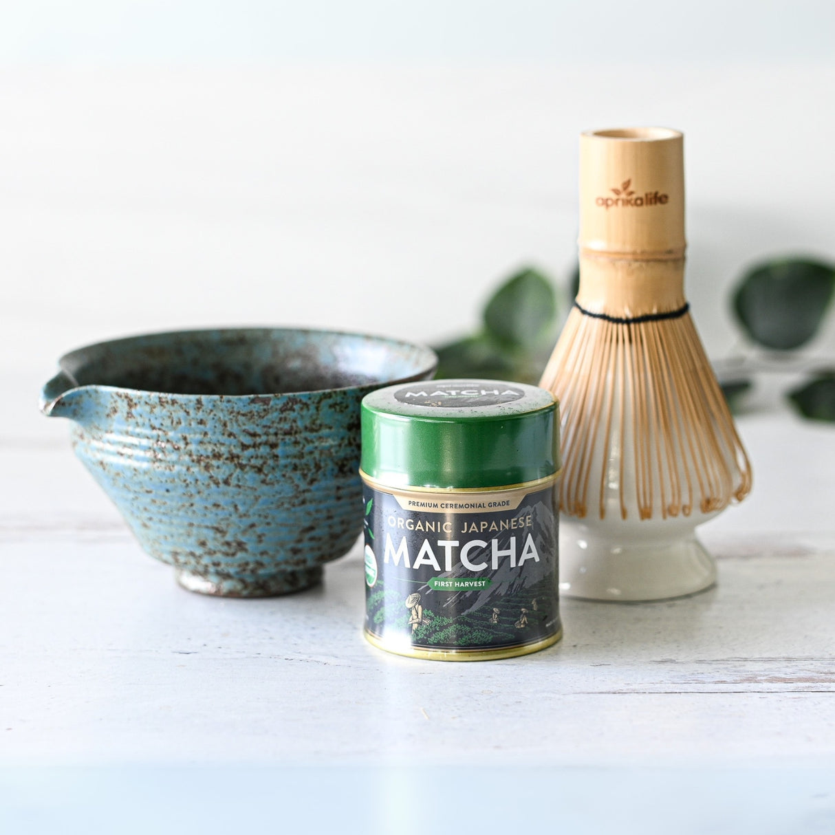The Blue Textured Ceramic Matcha Bowl with Spout, an organic Japanese matcha tin, and a bamboo whisk on a light surface make an ideal set for a Japanese tea ceremony or a sophisticated housewarming gift.