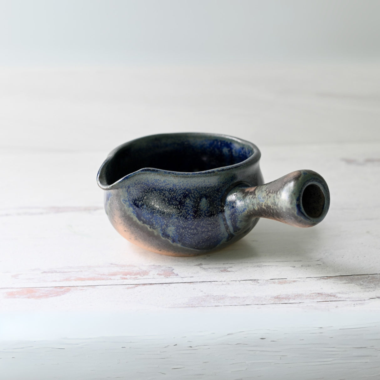 The Blue Spouted Ceramic Matcha Bowl, part of the Organic Japanese Matcha Set, rests elegantly on a white wooden surface with its spout and handle.