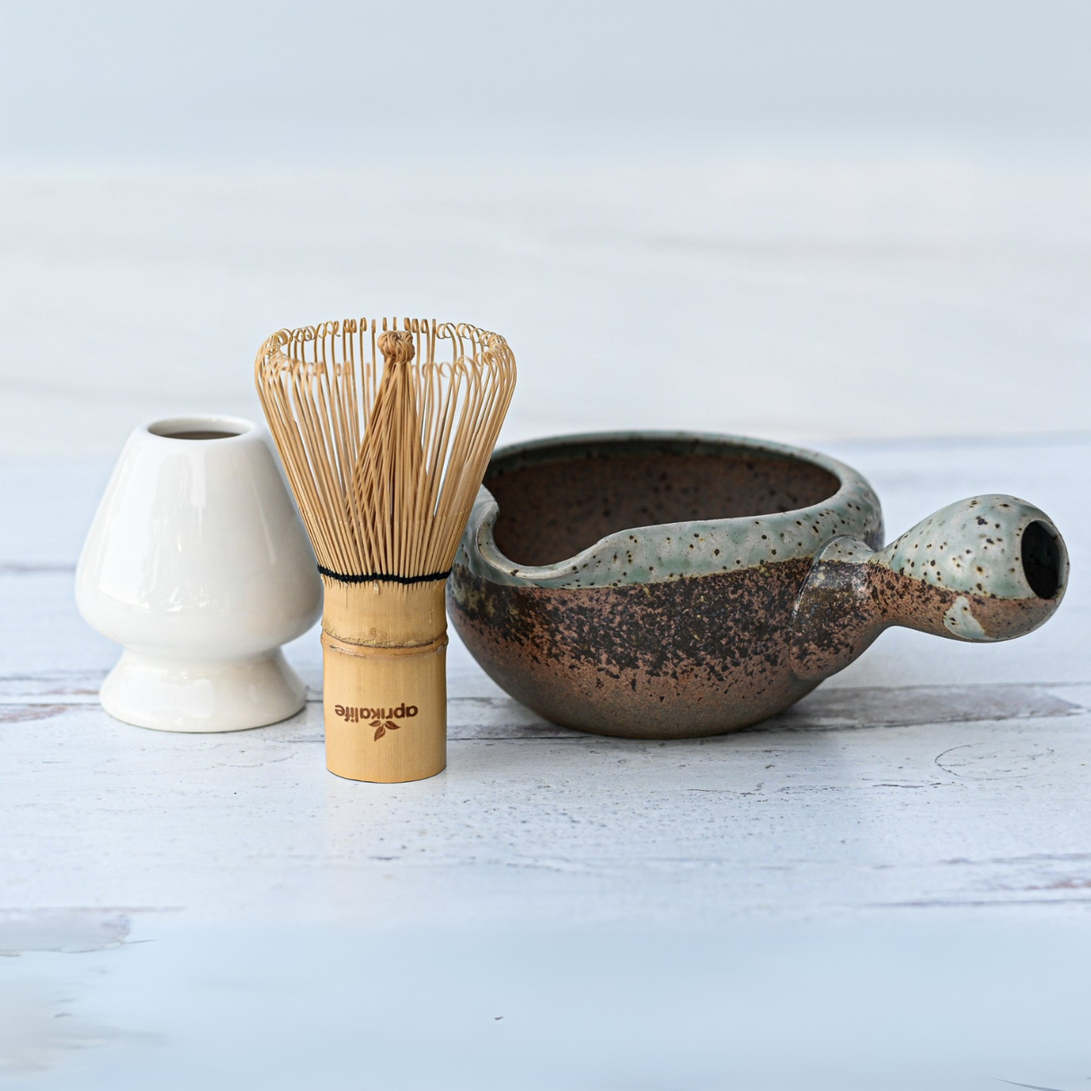 The Brown Ceramic Matcha Bowl with Spout, Bamboo Matcha Whisk, Whisk Holder, and Organic Japanese Matcha Set is ideal for preparing authentic matcha in the traditional Japanese tea ceremony on a light wooden surface.