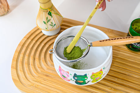Hand-sift matcha into a kawaii cat bowl on a wooden trayβjust add a bamboo whisk from the White Unfurl Matcha Gift Set for the ultimate tea experience.