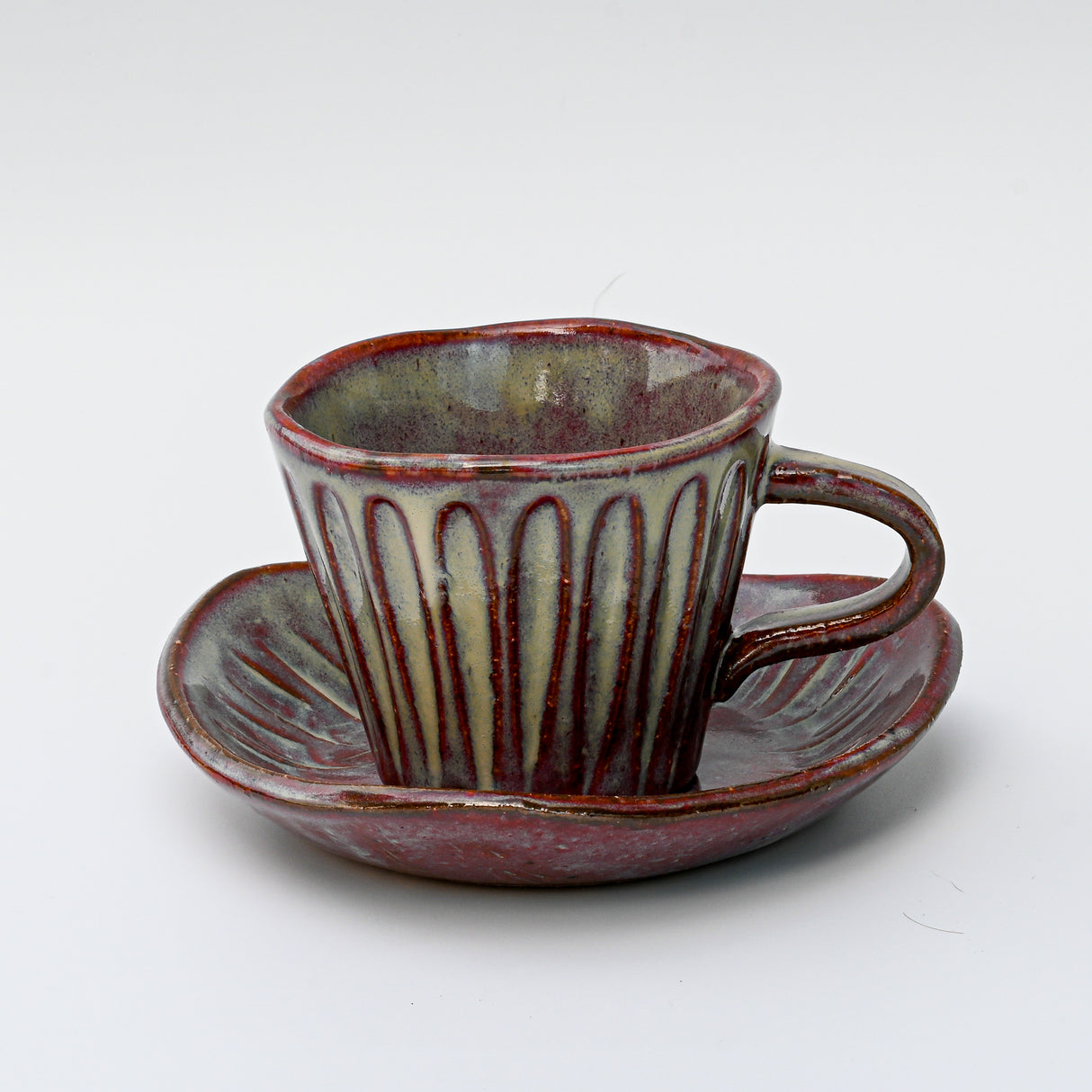 The Shibu Yunomi Japanese Tea Cup with Saucer, featuring a maroon and gray glaze on white, showcases exquisite Japanese craftsmanship. As a piece of Minoyaki pottery, it highlights the elegance found in handmade art.