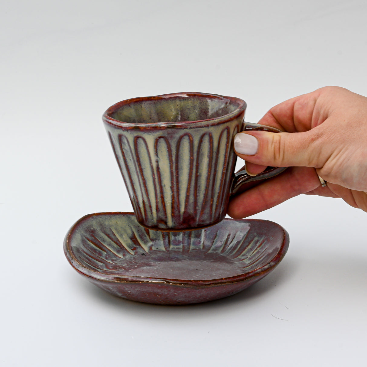 A hand holds a Shibu Yunomi Japanese Tea Cup over its matching saucer, highlighting the elegance of Minoyaki pottery against a pristine white background.