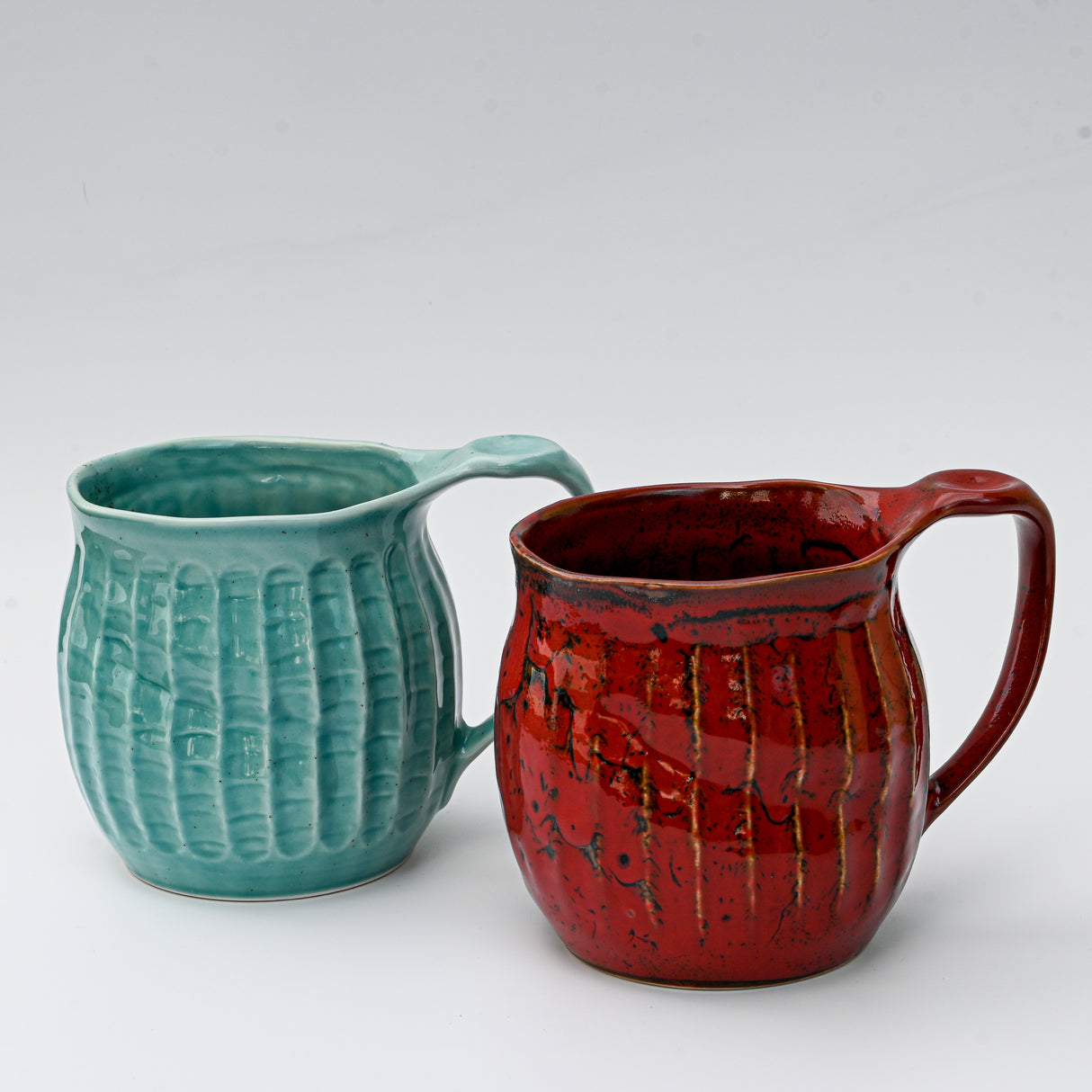 Two handmade Japanese ceramic mugs, one in vibrant red (18oz) and the other in teal, both feature an elegant ridged design. Set against a plain backdrop, these textured mugs make a striking display for tea or coffee enthusiasts.