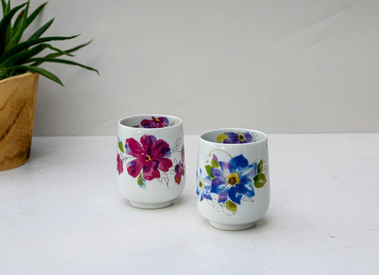 A Pink Flower Waisted Tea Cup with a red and blue floral design, made using traditional Japanese ceramic techniques, sits on a light surface near a potted plant.