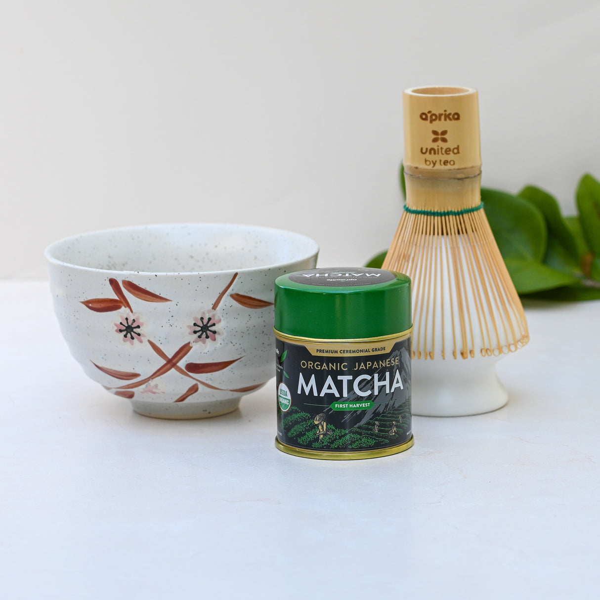 The Bamboo Matcha Bowl, with a Bamboo Matcha Whisk and Whisk Holder Set, elegantly paired with a tin of organic Japanese matcha on a light surface creates the ideal matcha tea set.