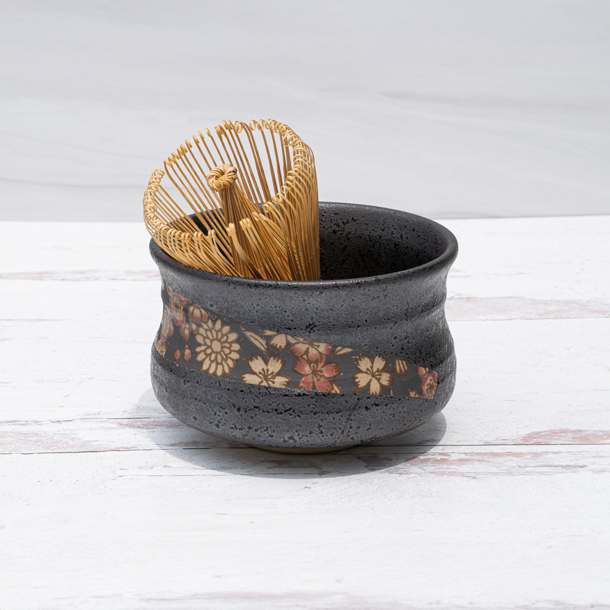 Black with Flowers Matcha Bowl and bamboo whisk on a white wooden surface.