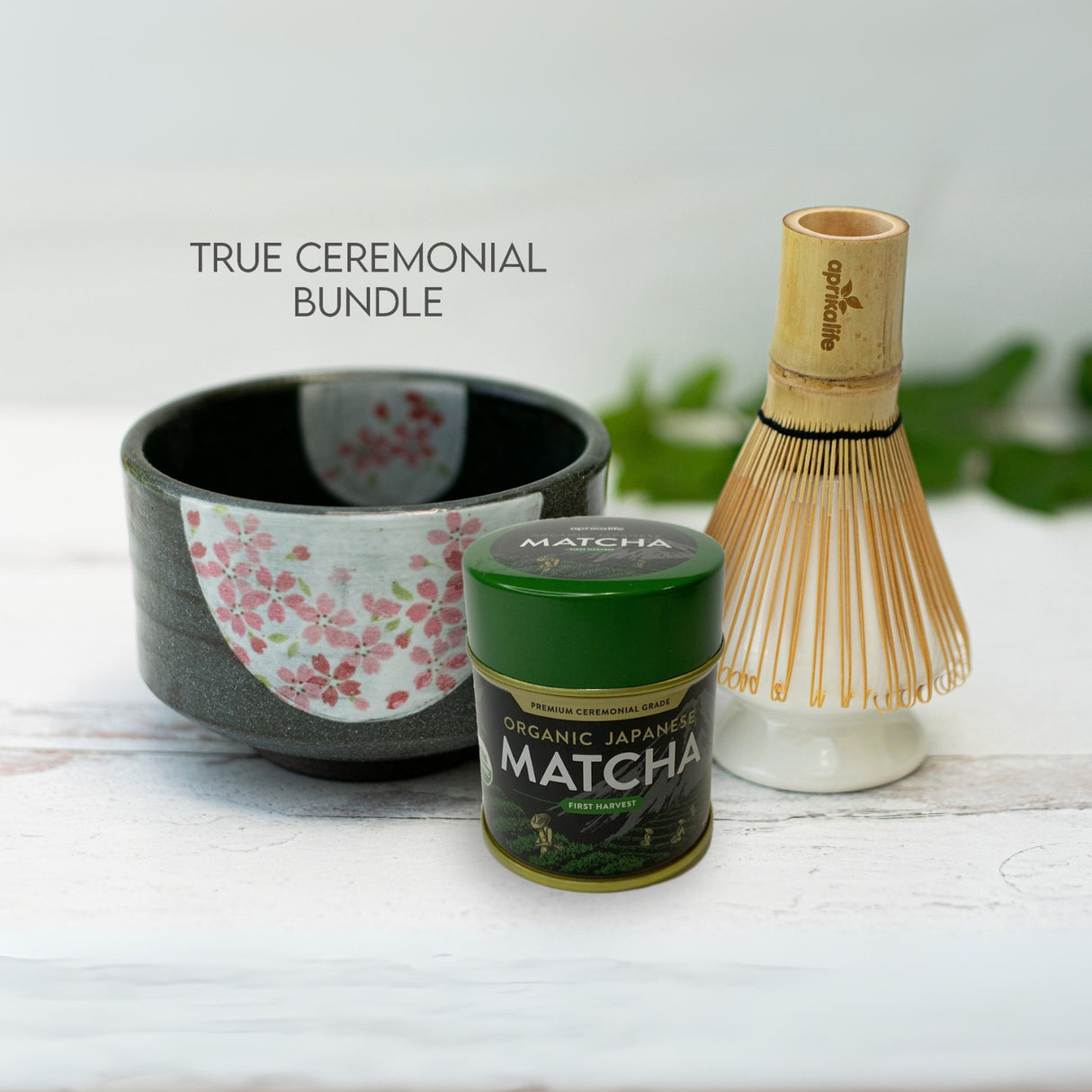 The Dark Grey Flowers Ceramic Matcha Bowl elegantly pairs with a matcha container and bamboo whisk on a white surface.