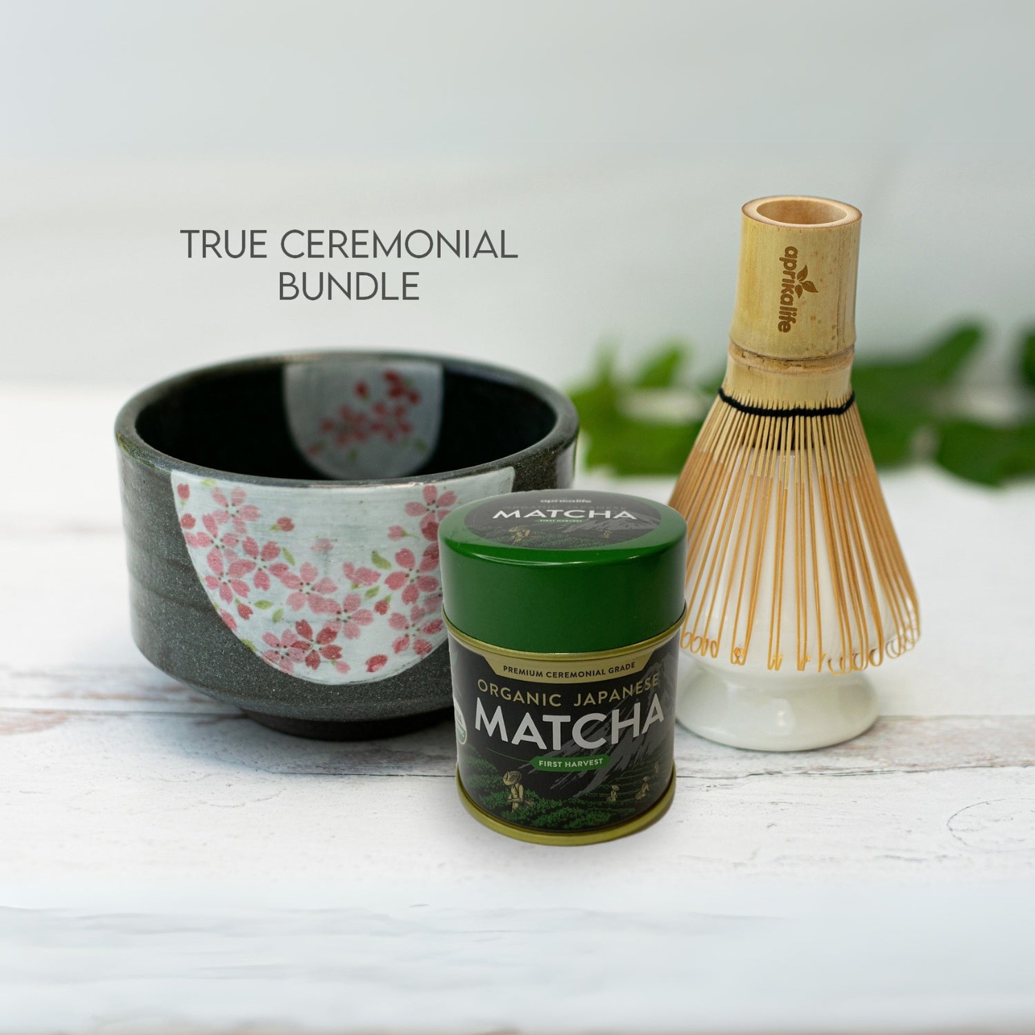 The Dark Grey Flowers Ceramic Matcha Bowl elegantly pairs with a matcha container and bamboo whisk on a white surface.