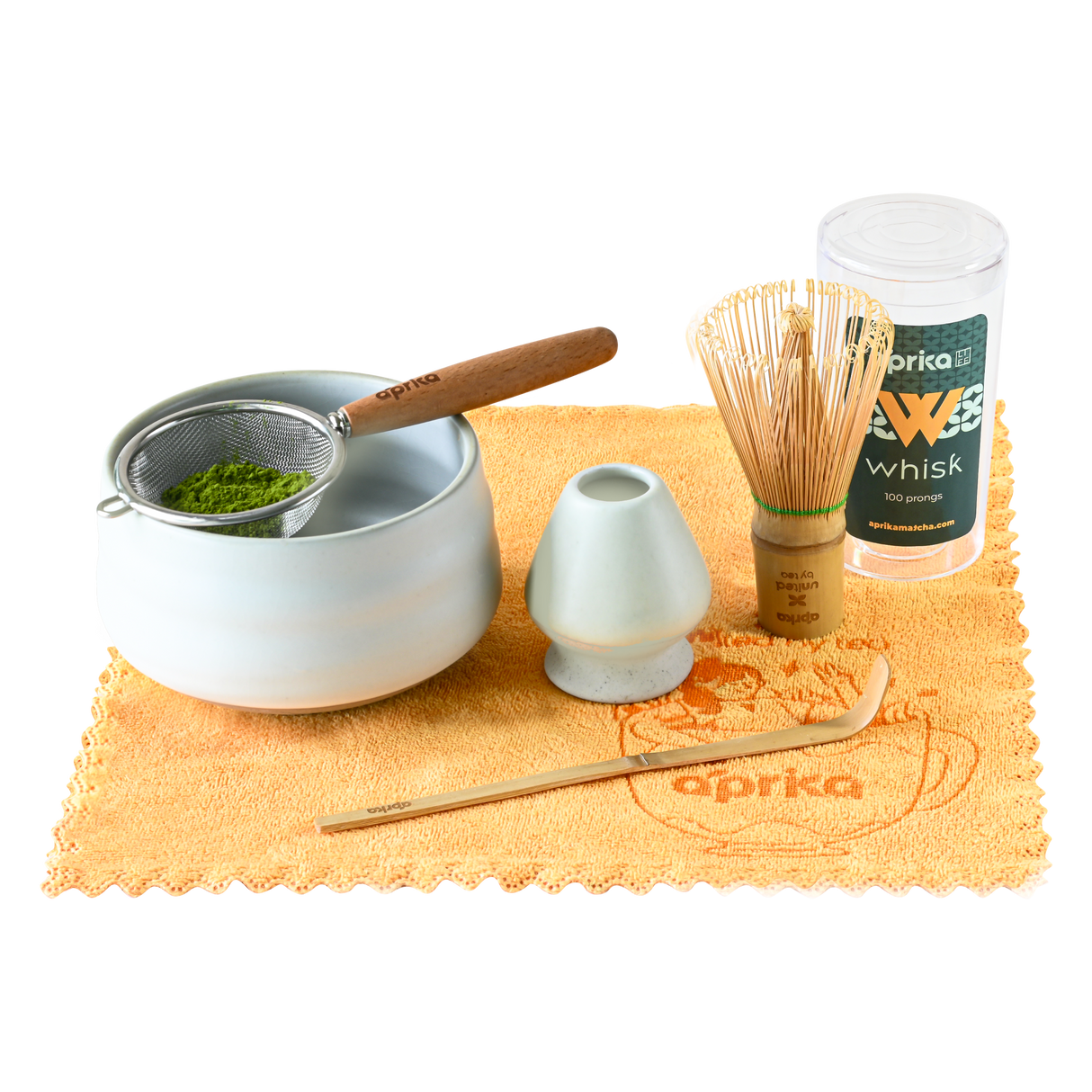 Ceremonial Matcha Starter Kit - Ivory White includes a ceramic matcha bowl, bamboo whisk, sifter, scoop, and holder artistically arranged on a yellow cloth.