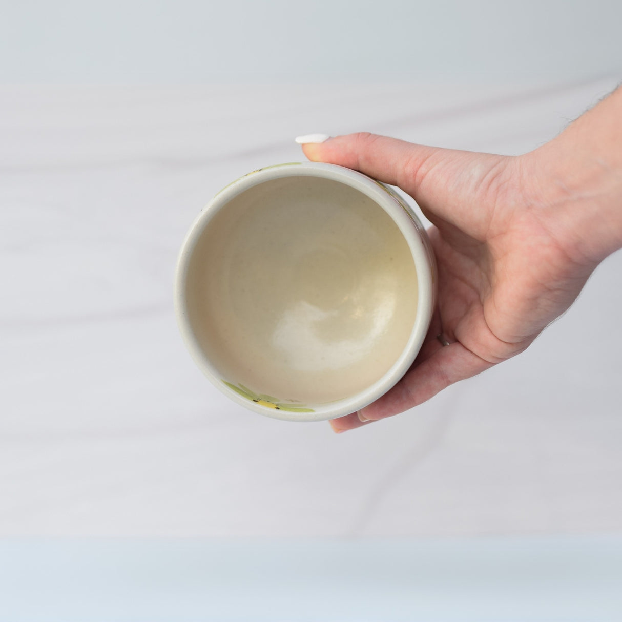 A hand holds the Green Flowers Ceramic Matcha Bowl from the Matcha Set, featuring Japanese-inspired pottery, against a light background.