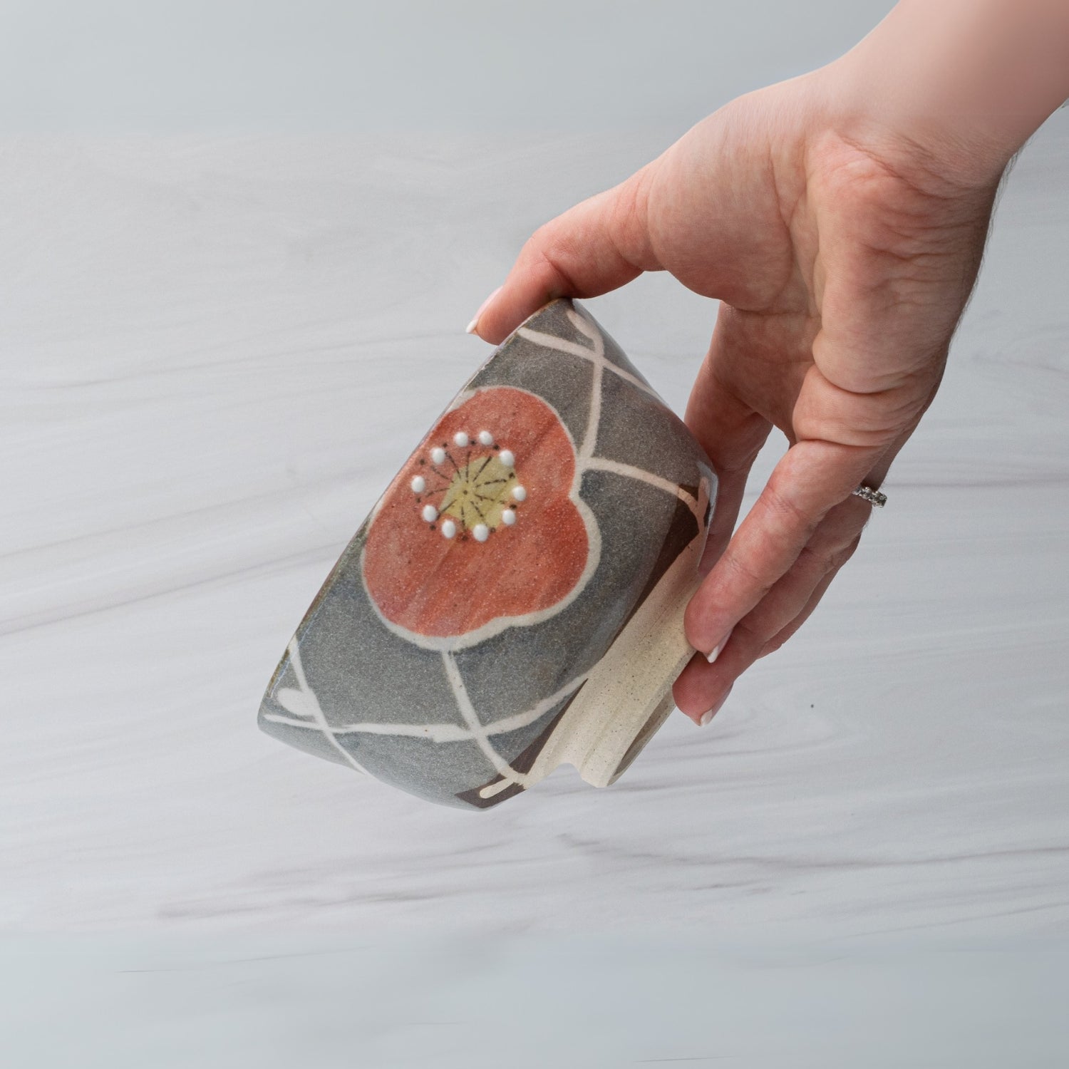 A hand holds the Gray with Flowers Ceramic Matcha Bowl, part of a set with a bamboo matcha whisk and whisk holder—a stylish upgrade to your tea accessories.