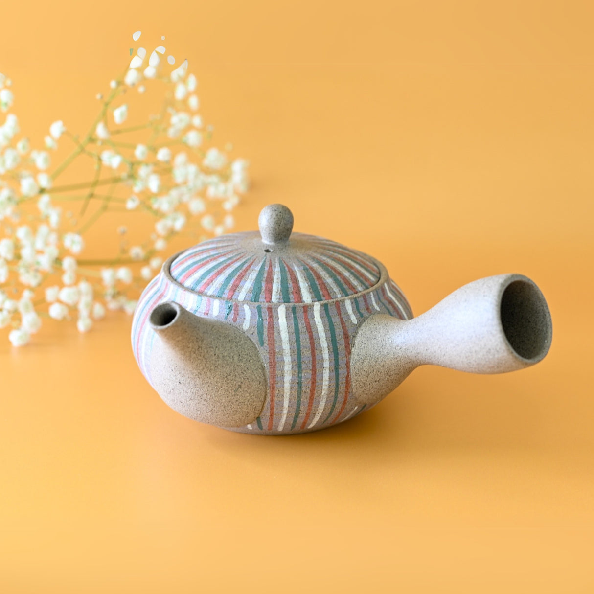 The Handcrafted Japanese Kyusu Teapot with Filters (310ml) features two spouts and a handle, set against a yellow background with white flowers, highlighting the elegance of Japanese ceramics.