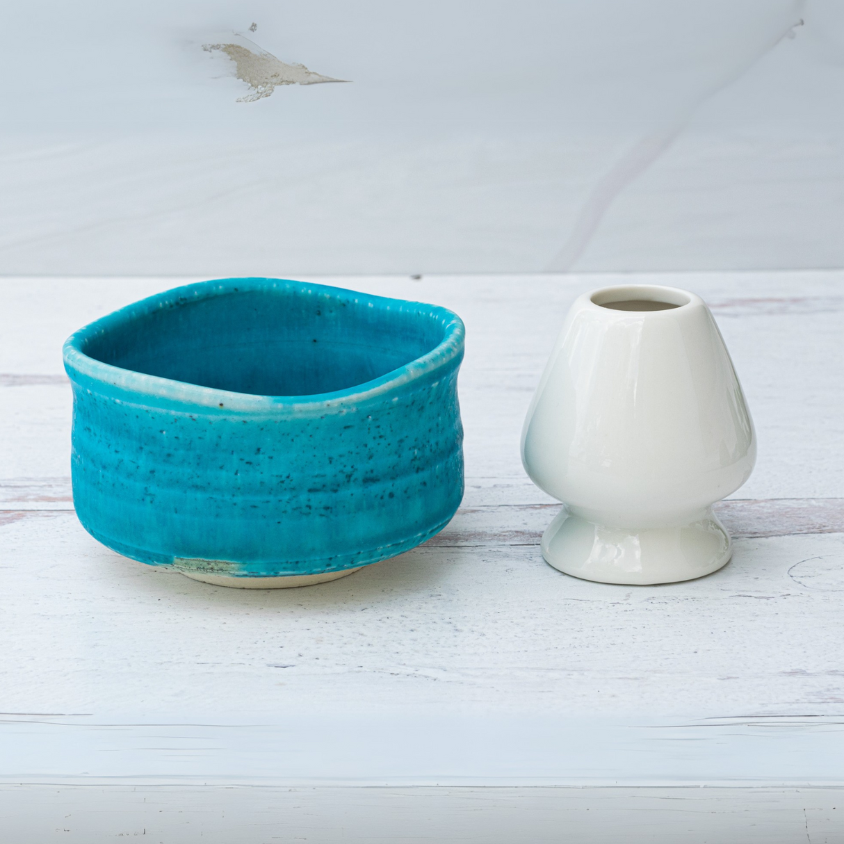 An Iguchi Blue Matcha Bowl and a white vase adorn the light wooden surface, showcasing exquisite Japanese pottery.