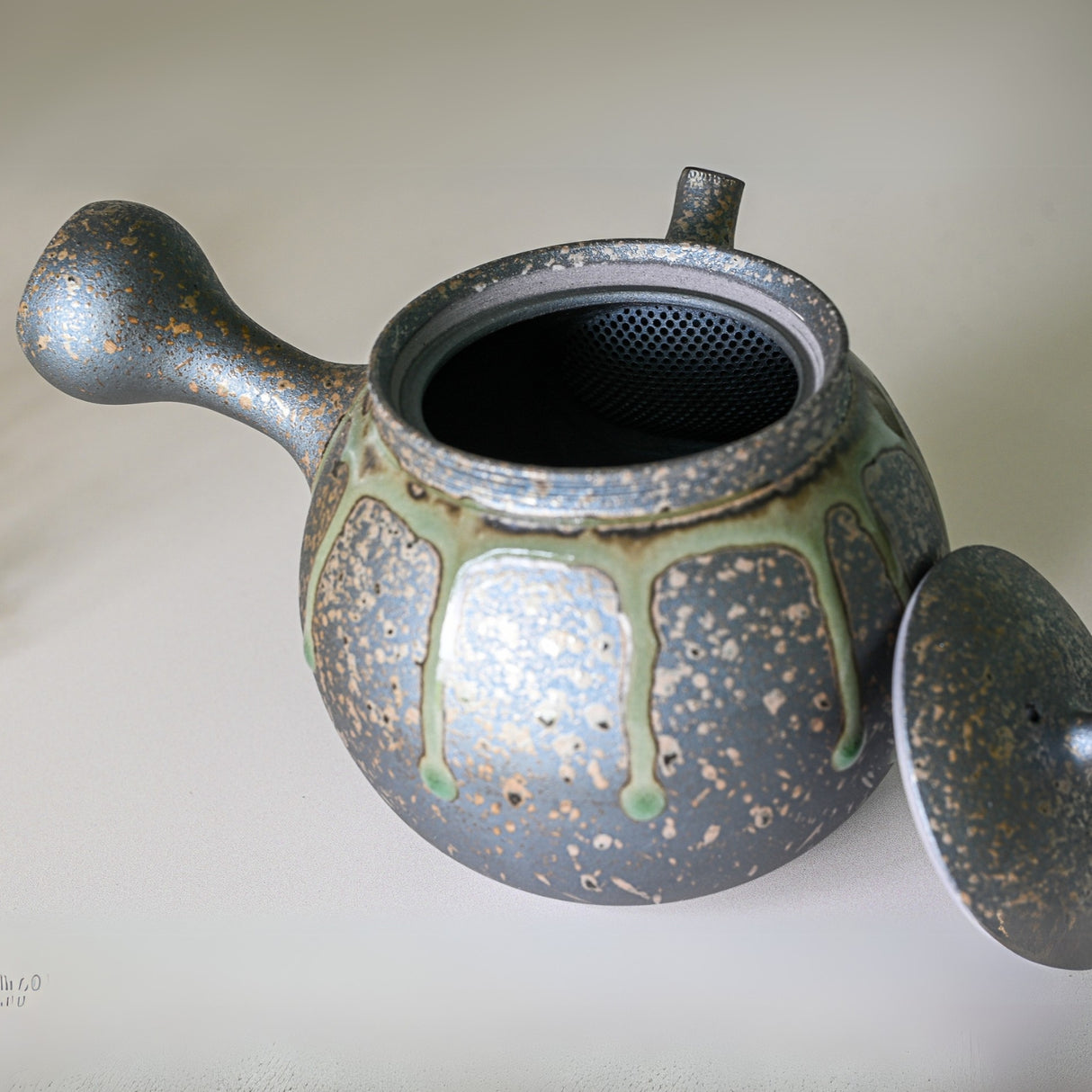 The Japanese Kyusu Set teapot, with its lid off, displays a textured, speckled blue and green glaze reminiscent of Tokoname ceramics artistry.