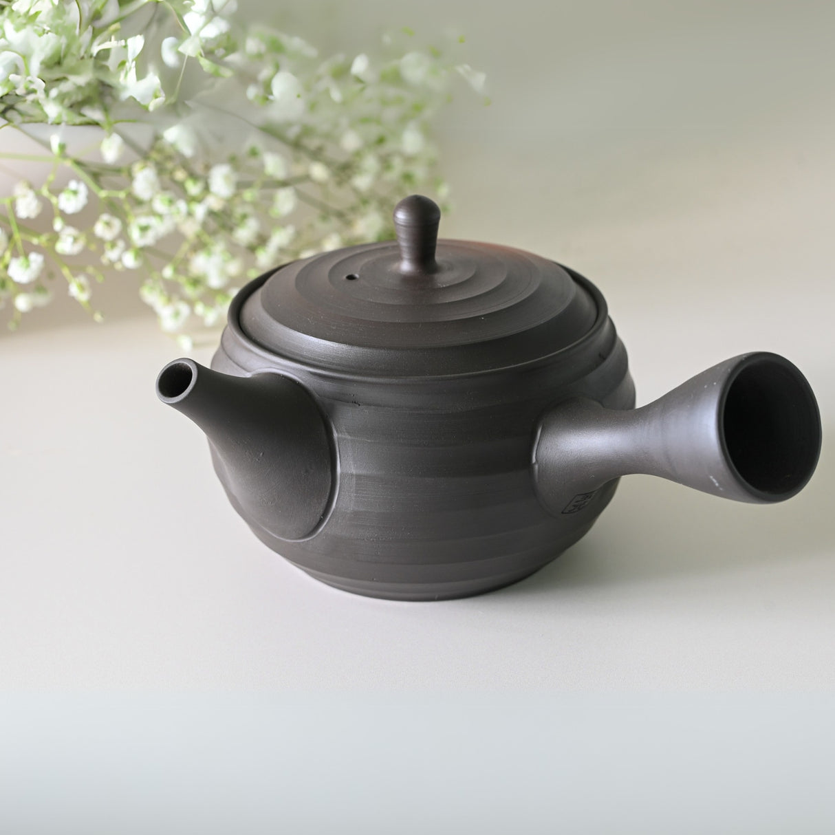The Japanese Kyusu Set teapot (270ml) with filters, in black, sits elegantly on the table, perfectly complemented by white flowers.
