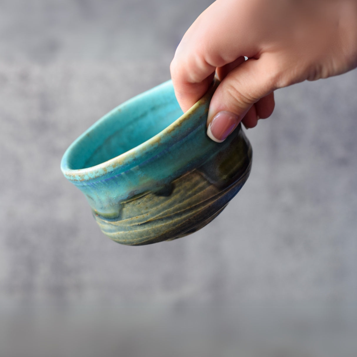 A hand gracefully holds the Marusho Blue Matcha Bowl against a gray background, highlighting the exquisite beauty of Minoyaki Japanese pottery.