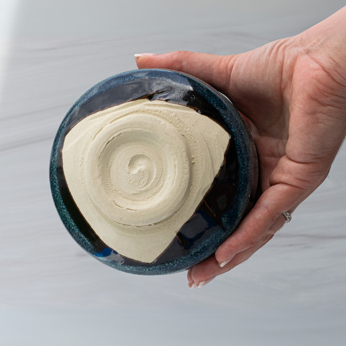A hand cradles the Maruyoshi Navy Sea Ceramic Matcha Bowl, with its unglazed spiral bottom providing an earthy contrast to the glossy blue glaze, evoking a serene tea ritual.