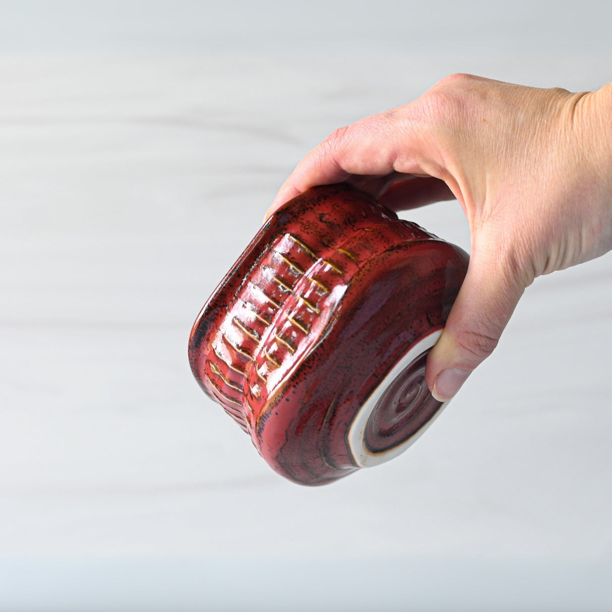 A hand holds a Meisen Red Matcha Bowl, showcasing its textured red ceramic design with a white base, against a light background.