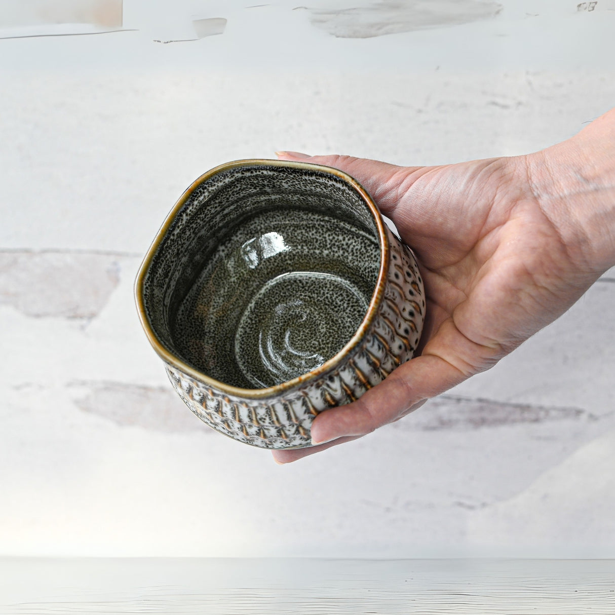 A hand cradles the White Ceramic Meisen Matcha Bowl, featuring a textured, speckled exterior inspired by classic Minoyaki pottery, against a light background.