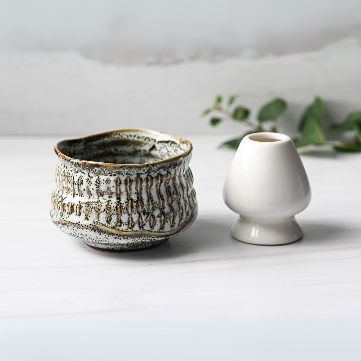 The White Ceramic Meisen Matcha Bowl, Bamboo Matcha Whisk, Whisk Holder, and Organic Japanese Matcha Set sits on a light surface, creating a serene matcha tea setting.