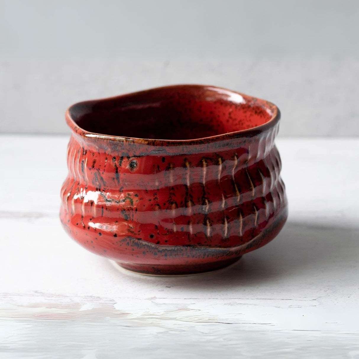 A red Minoyaki matcha bowl with a wavy rim rests on a light wood surface, paired with a bamboo whisk from the Organic Japanese Matcha Set.