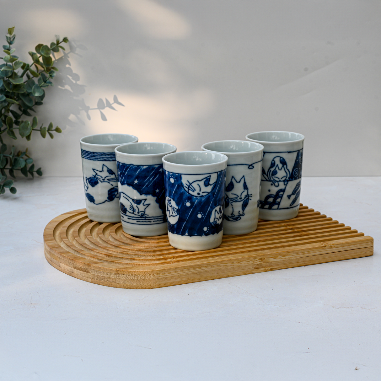 A set of 5 adorable blue & white Mino-ware cat tea cups (180ml each) is arranged on a wooden tray, with greenery in the background.