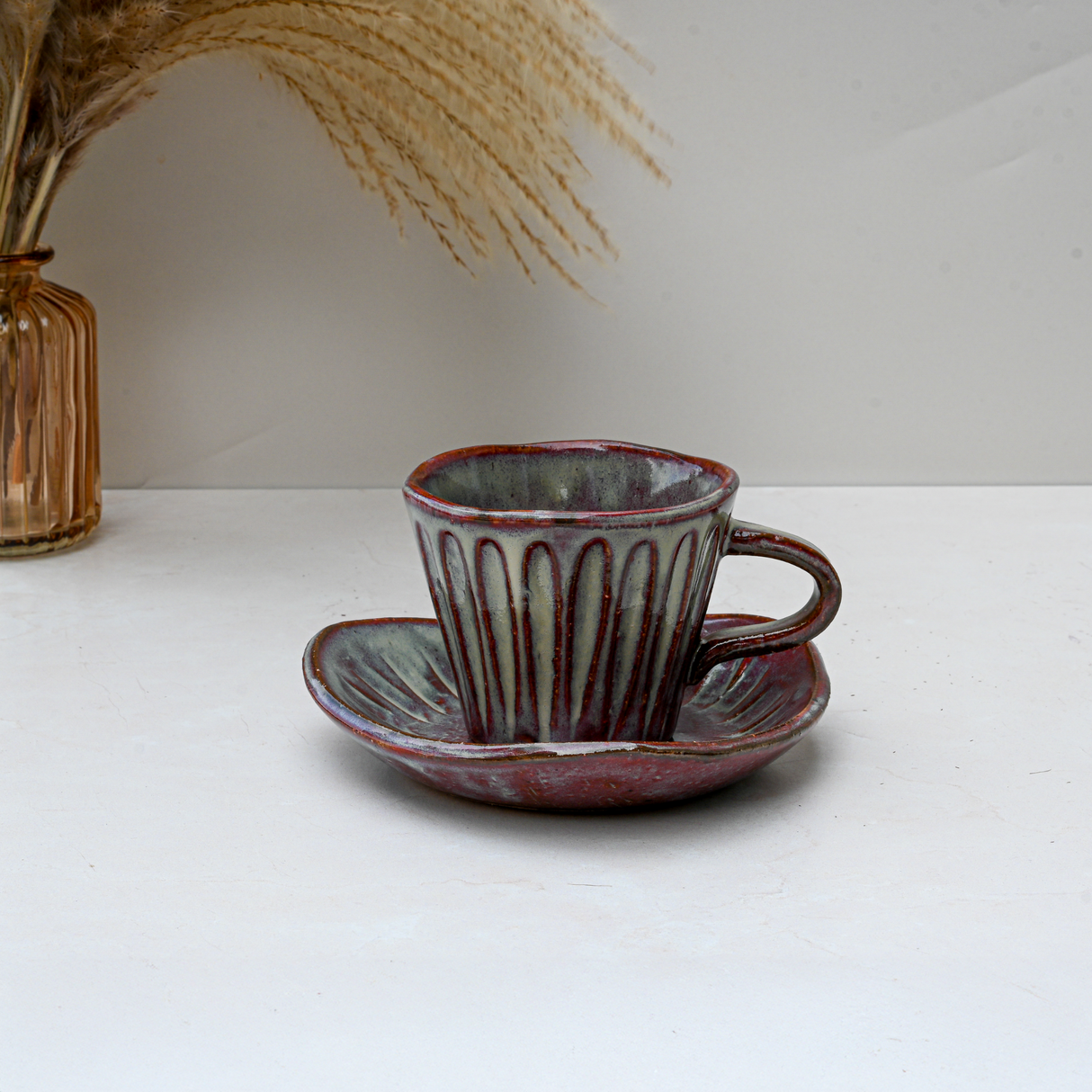 The Shibu Yunomi Japanese Tea Cup with Saucer features a brown and gray vintage-inspired design, displayed on a white surface beside dried plants.