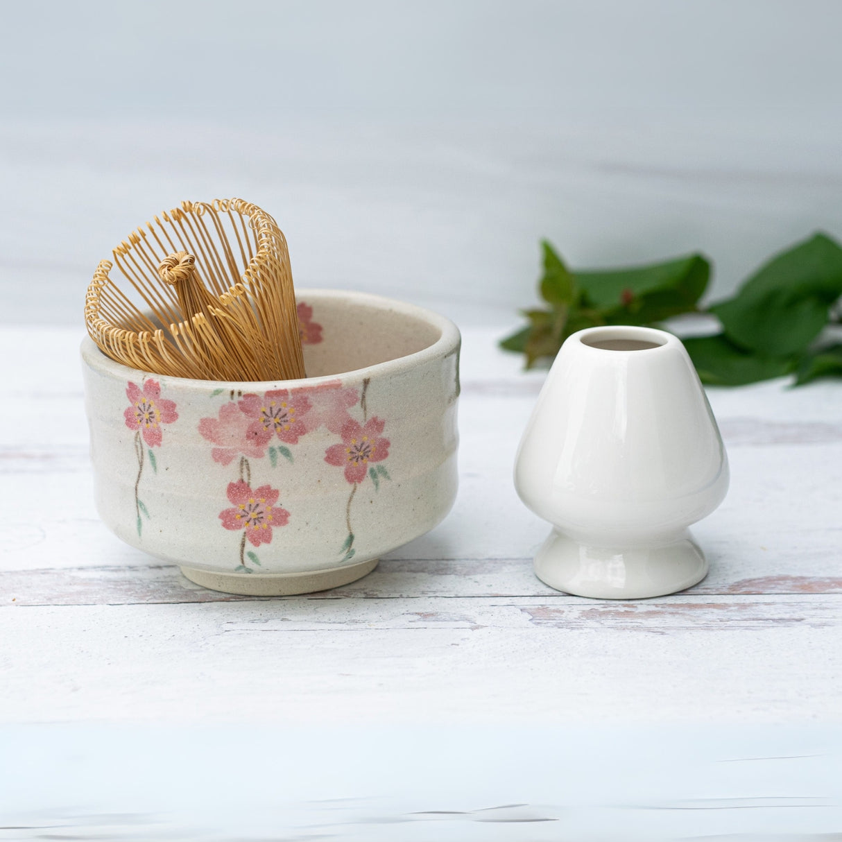 The Pink Sakura Flowers Ceramic Matcha Bowl, Bamboo Matcha Whisk, Whisk Holder, and Organic Japanese Matcha Set create a refined Japanese teaware display on a light wooden surface.