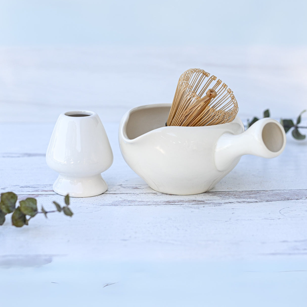 White Ceramic Matcha Bowl with Spout set on a white wooden surface, beautifully accented with eucalyptus sprigs. An ideal housewarming gift inspired by the Japanese tea ceremony.