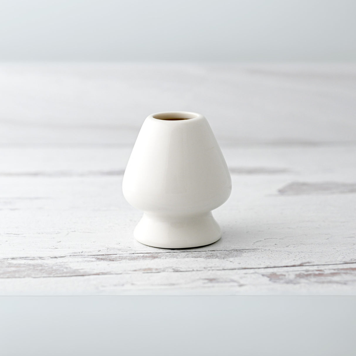 A White Matcha Whisk Holder from the Bamboo Whisk Set rests gracefully on a light wooden surface, embodying the elegance of a tea ceremony accessory.