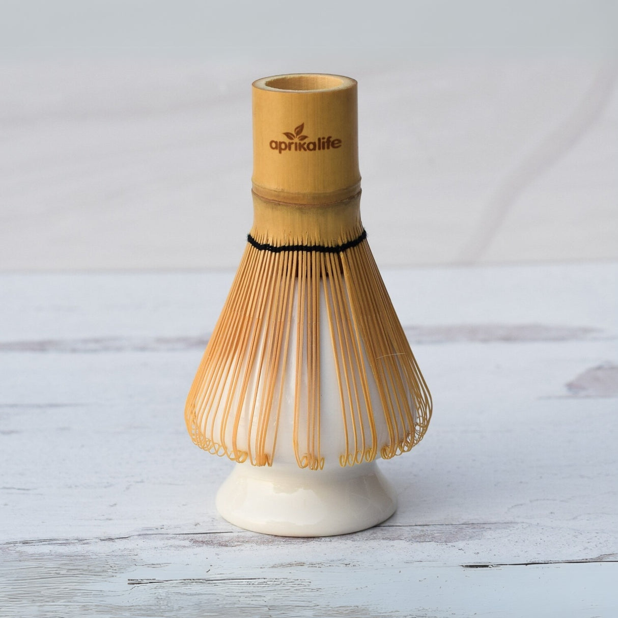 The White Matcha Whisk Holder and Bamboo Whisk Set features a branded bamboo whisk standing elegantly on a white surface, paired with a chic ceramic holder—ideal for tea ceremonies.