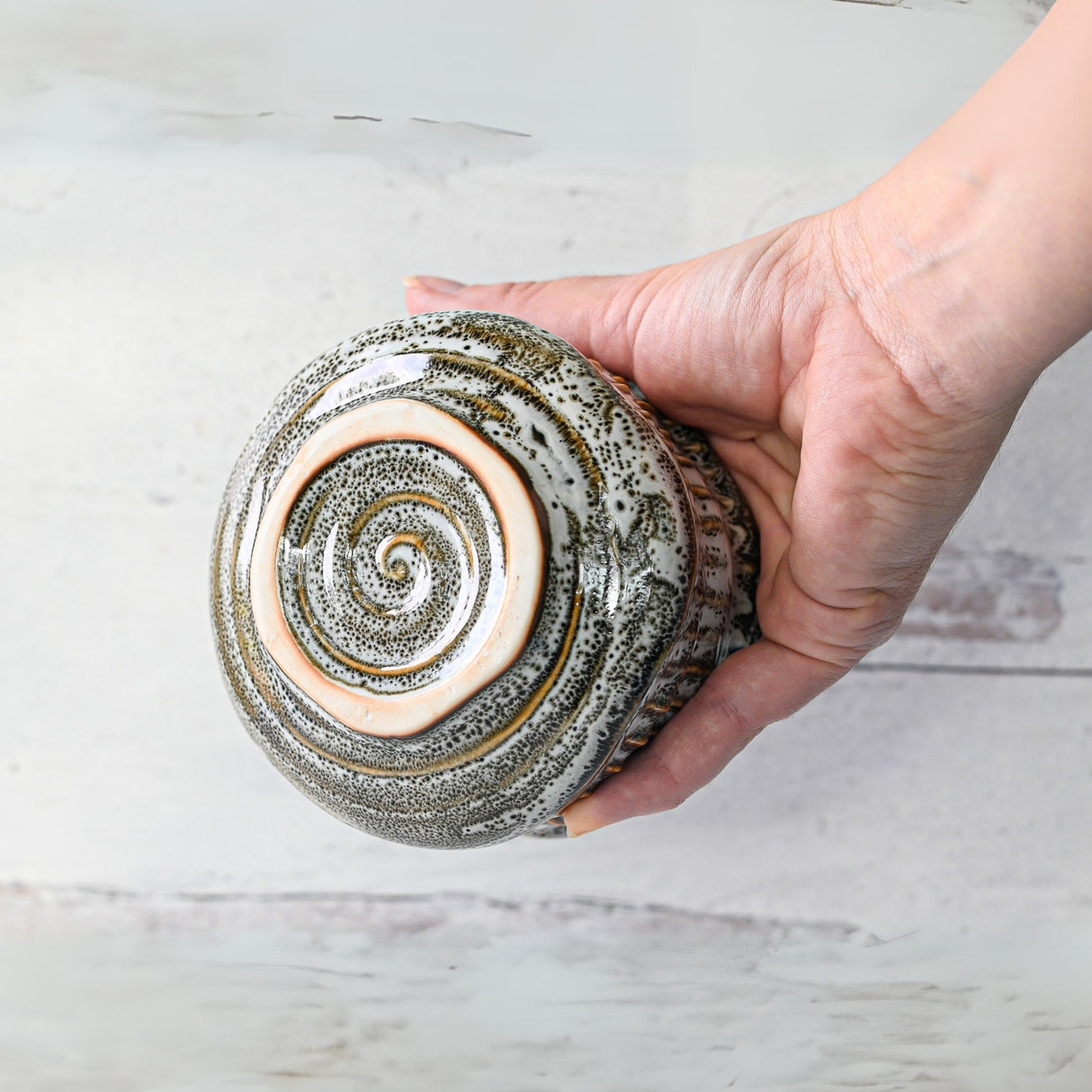 A hand gently cradles the White Ceramic Meisen Matcha Bowl, featuring a spiral pattern at its base, set against a light background.