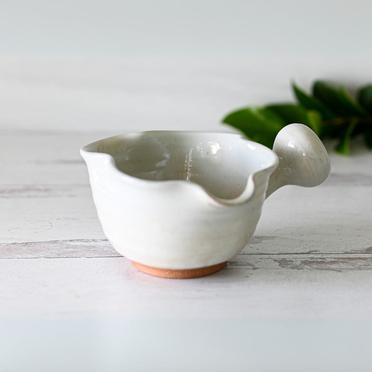 The "White Wavy Ceramic Matcha Bowl with Spout and Optional Set," featuring an irregular shape and handle, sits on a light wooden surface.