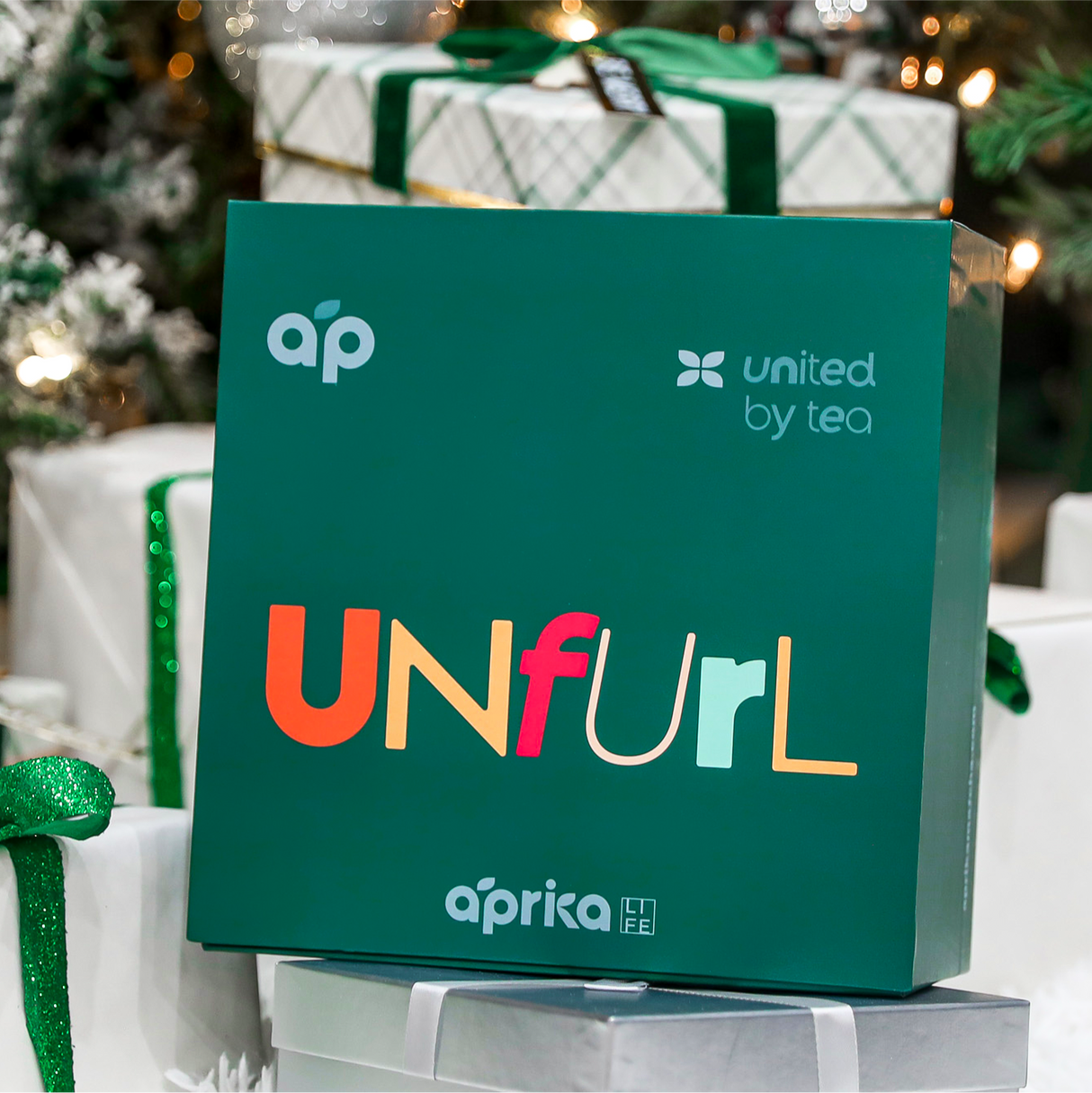 A festive green box with vibrant "UNFurl" text, wrapped gifts, and a decorated tree reveals the joy of the Ceremonial Matcha Starter Kit - Ivory White, featuring a Ceramic Matcha Bowl and Bamboo Whisk for a delightful experience.