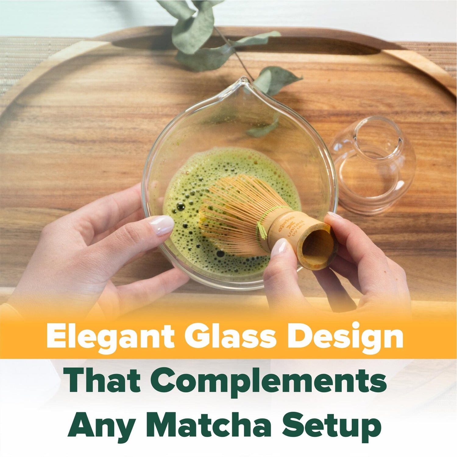 Hands whisking matcha in a glass bowl on a wooden tray, featuring the Clear Glass Matcha Whisk Holder and Bamboo Whisk Set for an elevated tea experience.