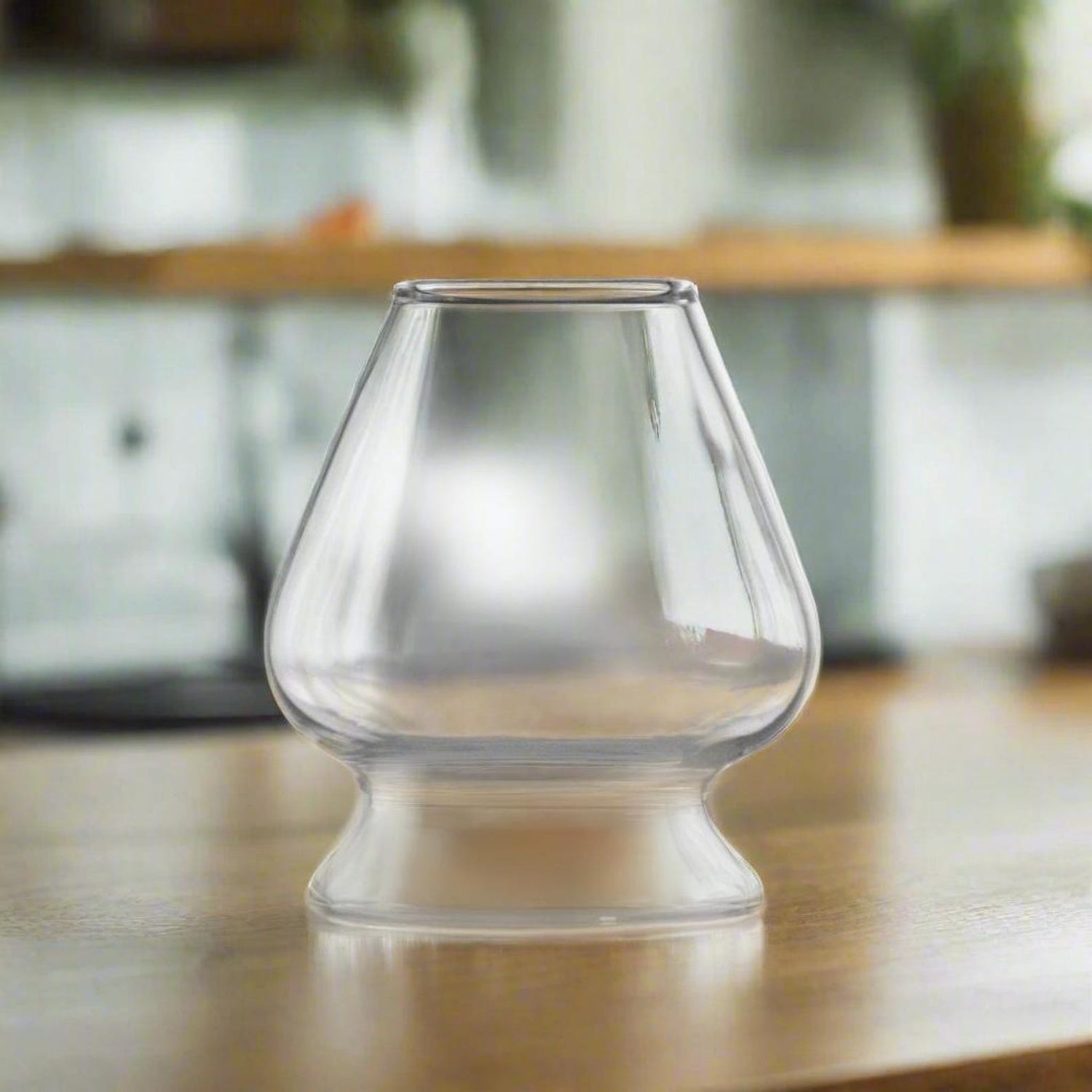 The Clear Glass Matcha Whisk Holder and Bamboo Whisk Set features a uniquely shaped borosilicate holder displayed on a wooden surface with a blurred kitchen background.