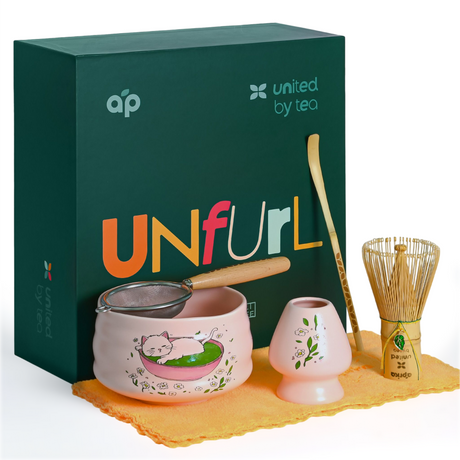 Pink Unfurl Matcha Gift Set with Bamboo Whisk, Cat Print Bowl, strainer, scoop, cup, and a green "Unfurl" box featuring "united by tea" branding.